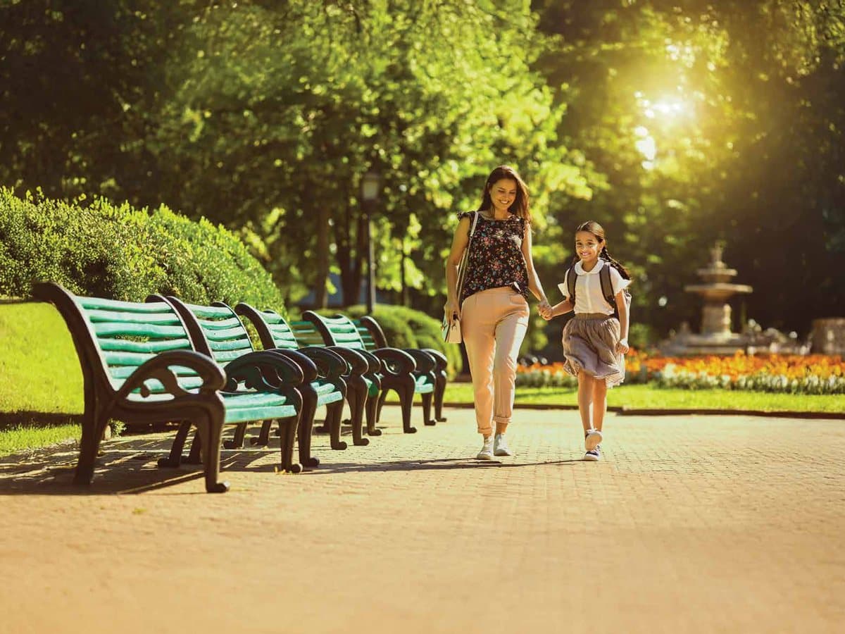 A mother and daughter walking through a sunlit park